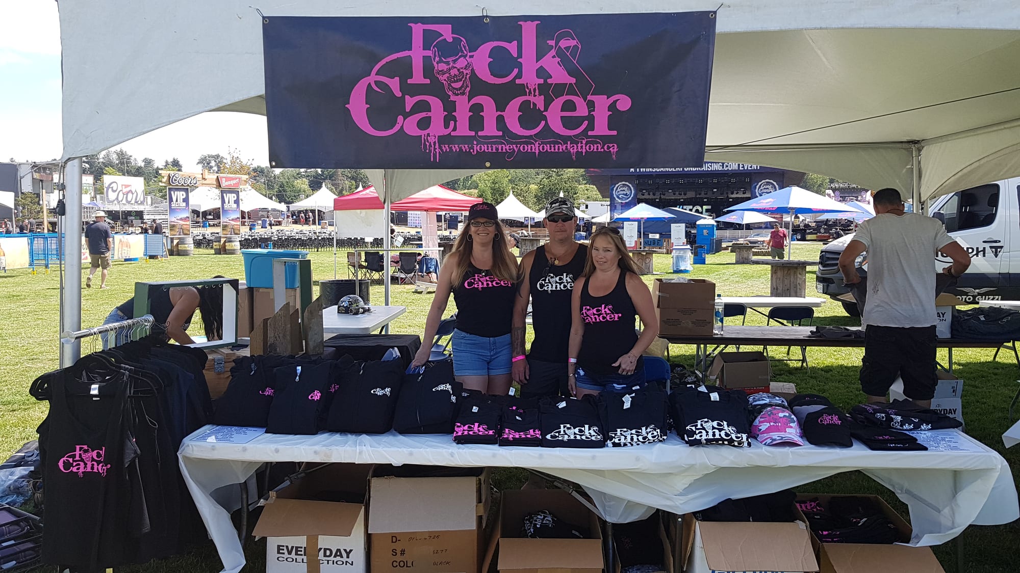 Three volunteers at an FCK Cancer merch tent at a festival