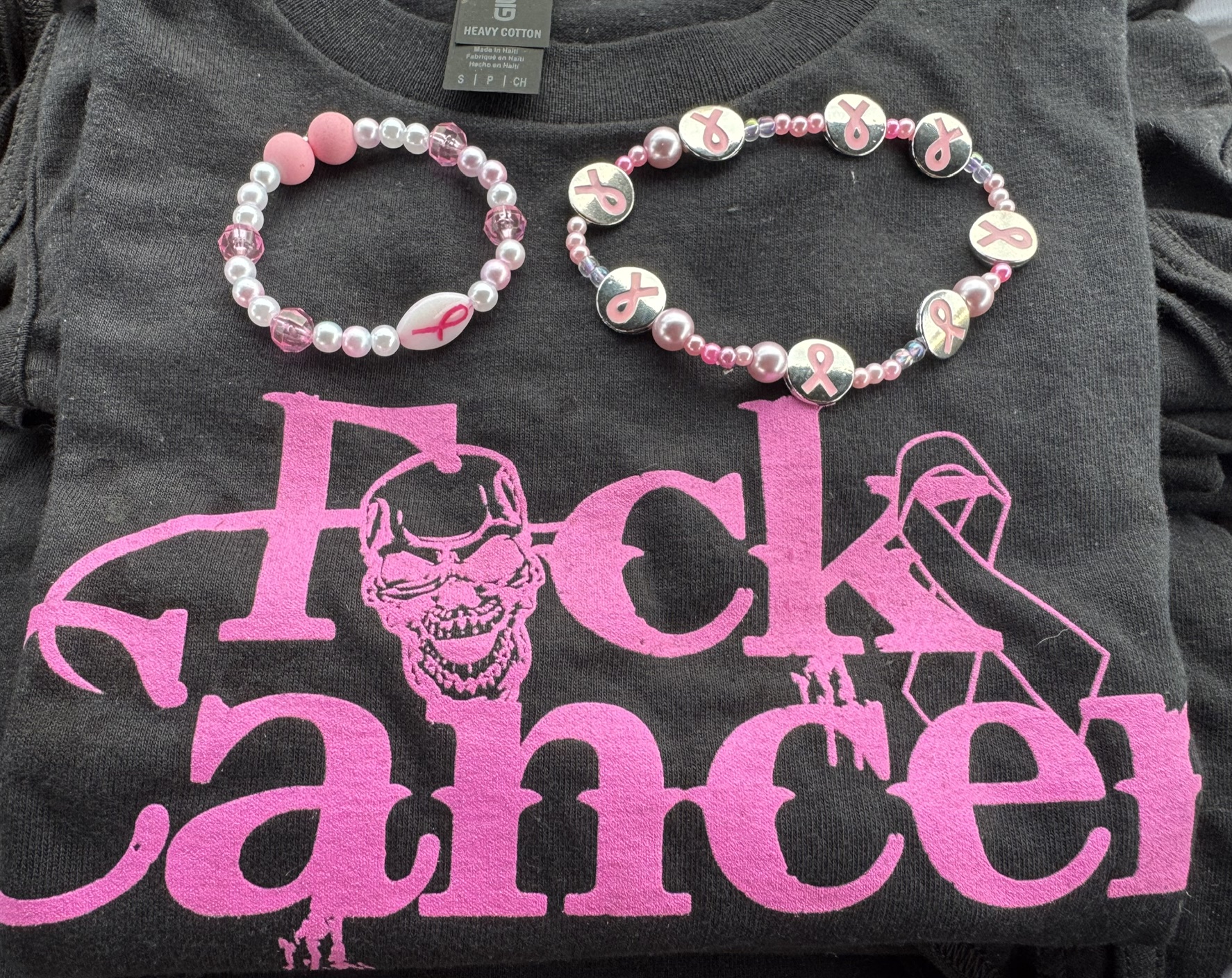 Two pink ribbon bracelets on a black FCK Cancer shirt